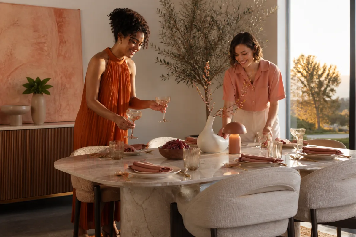 Two friends styling a sunny dining table with glassware and modern decor